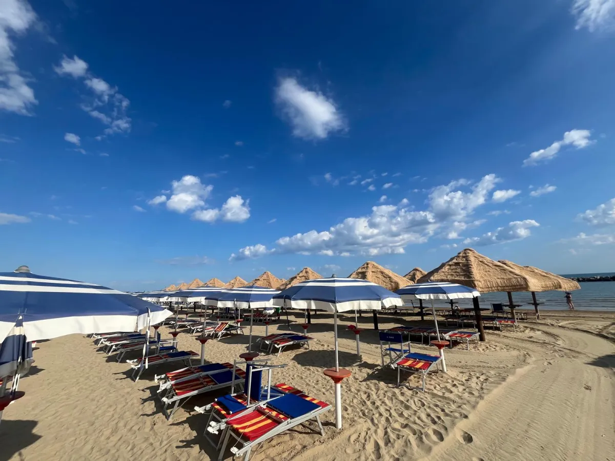 Lettini e ombrelloni a righe sulla spiaggia con palme di paglia sullo sfondo