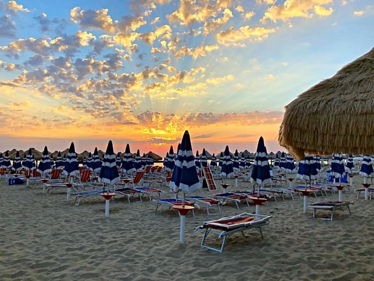 Tramonto dorato sulla spiaggia con ombrelloni chiusi in controluce