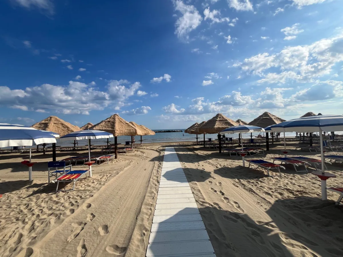 Passerella verso il mare tra ombrelloni in paglia e lettini