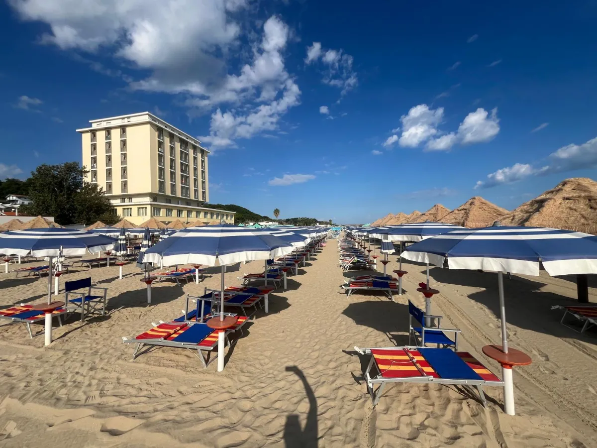 File di ombrelloni e lettini colorati con hotel sullo sfondo