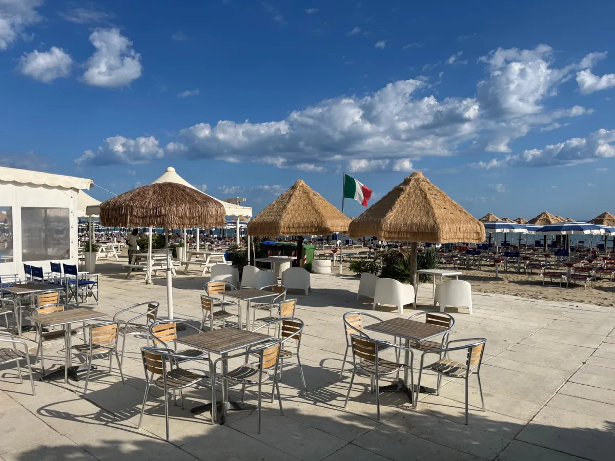 Area bar con tavolini, ombrelloni in paglia e bandiera italiana