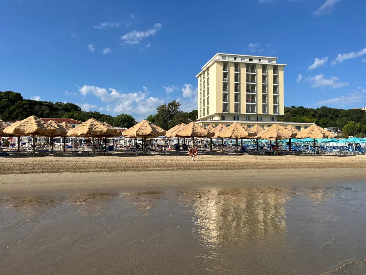 Panorama dalla riva con ombrelloni, hotel e riflessi sulla sabbia bagnata